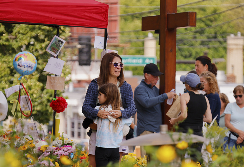 A child is embraced as people visit a makeshift memorial Aug. 29, 2025, at Annunciation Catholic Church in Minneapolis after the Aug. 27 shooting there during a Mass attended by students of the affiliated school. (AP photo/Bruce Kluckhohn)