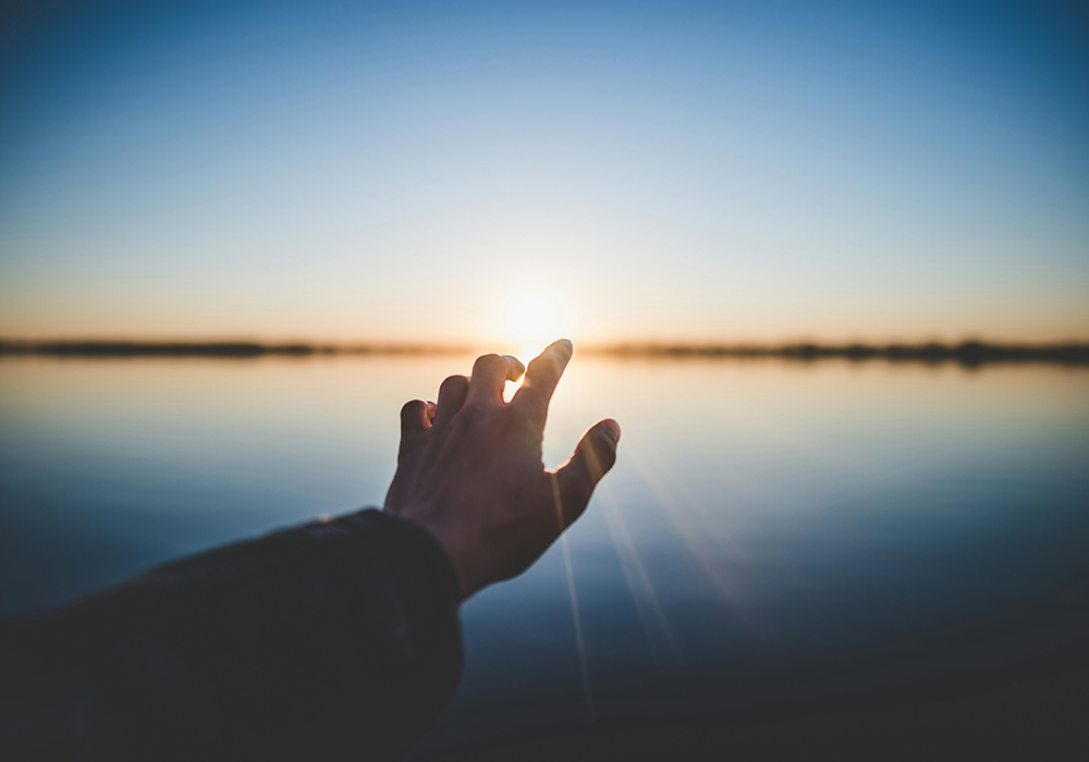 A photo illustration shows a hand outstretched toward a horizon. (Unsplash/Marc-Olivier Jodoin)