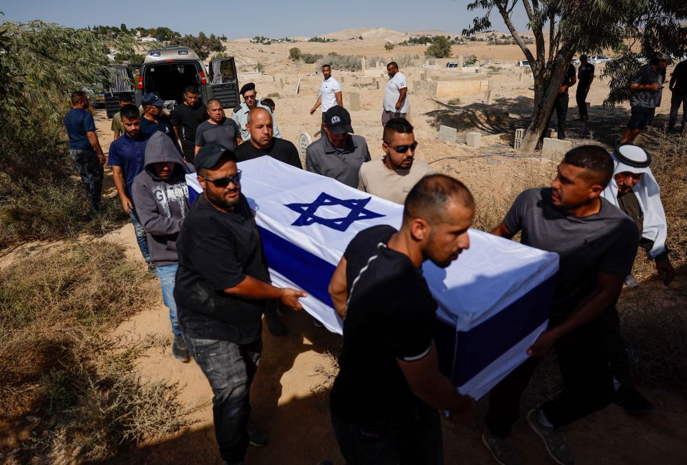 Pallbearers carry coffin draped with cloth with blue Star of David. 
