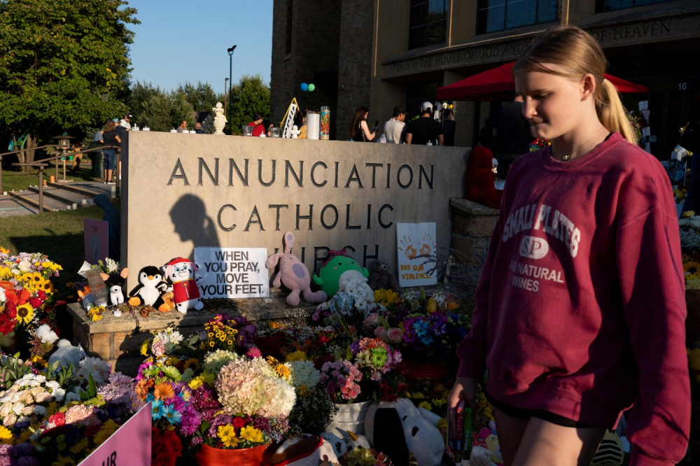 A young woman walks past a memorial outside Annunciation Church in Minneapolis Aug. 30, 2025, which is a home to an elementary school and was the scene of a shooting. The shooter opened fire with a rifle through the windows of the school's church and struck children attending Mass Aug. 27 during the first week of school, killing two and wounding 21 others. (OSV News/Reuters/Tim Evans)