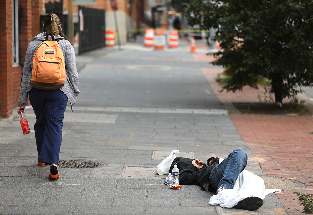 A woman walks past a homeless man sleeping on a sidewalk in Baltimore June 6, 2023. (OSV News/Bob Roller)