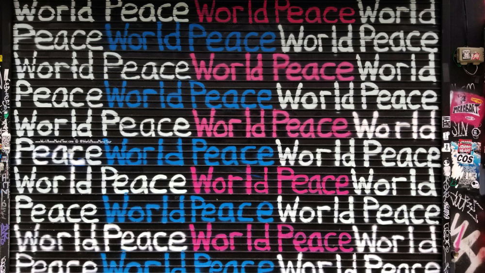 Graffiti with the words "World Peace" repeatedly written in white, blue and pink on a black background.