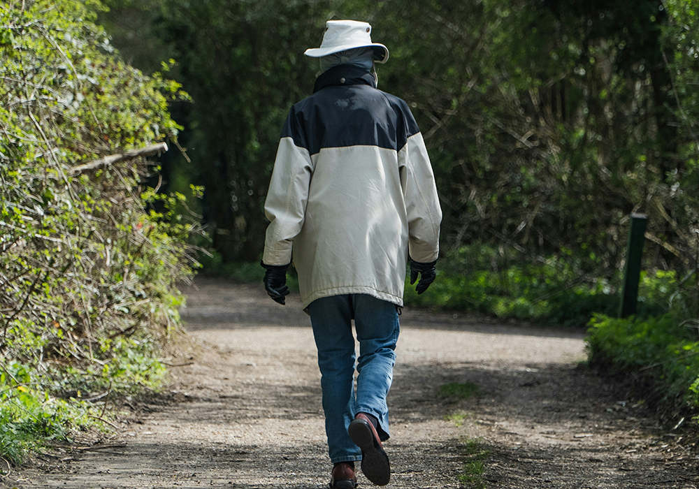 A person wearing a white jacket and a hat walks outside along a path. (Unsplash/Caspar Rae)