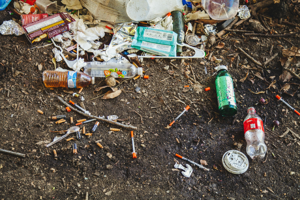 Dirty, empty used bottles and used needles scattered on the dirt ground.