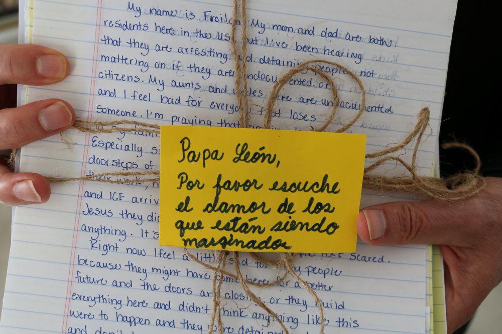 Bishop Mark Seitz holds a bundle of letters to Pope Leo XIV from migrants in the United States. Note, in Spanish, says, "Pope Leo, please listen to the cry of those who are being marginalized." 