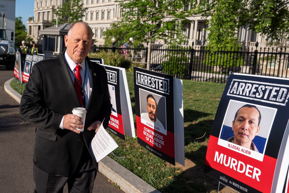 White House border czar Tom Homan walks to do a television interview at the White House April 28 in Washington. The signs show photos of people the Trump administration says are undocumented immigrants who have been arrested.