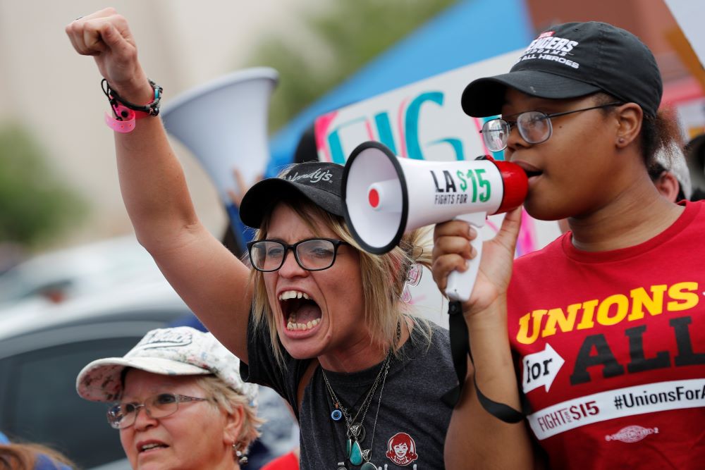 Woman wears T-shirt that says "Unions" and speaks into megaphone.