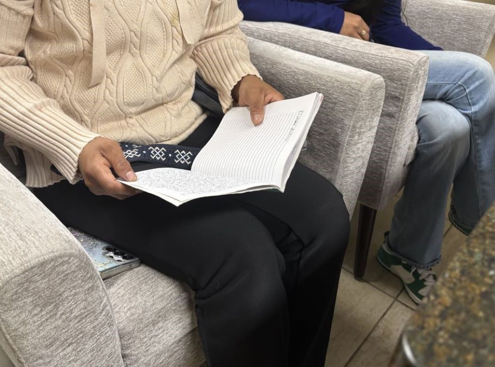 Two people sit in armchairs, ne with a notebook open.