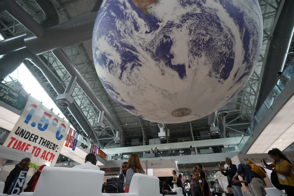 A big globe hangs from ceiling and signs calling for end to fossil fuels at COP30 room