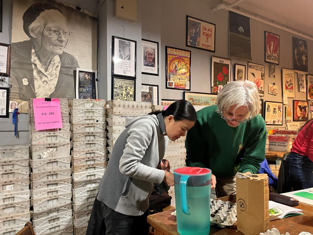 Members of the Catholic Worker's Integral Ecology Circle plant vegetable seedlings at the Maryhouse auditorium in New York City in March 2024. A photo of Dorothy Day, left, oversees the room. 