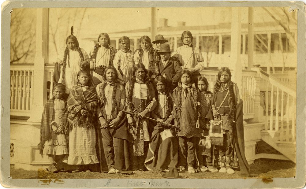 Nine male students and six female students pose on the steps of the bandstand on the Carlisle Indian Industrial School grounds in Carlisle, Pa., in March 1891, wearing the clothing they arrived in. 