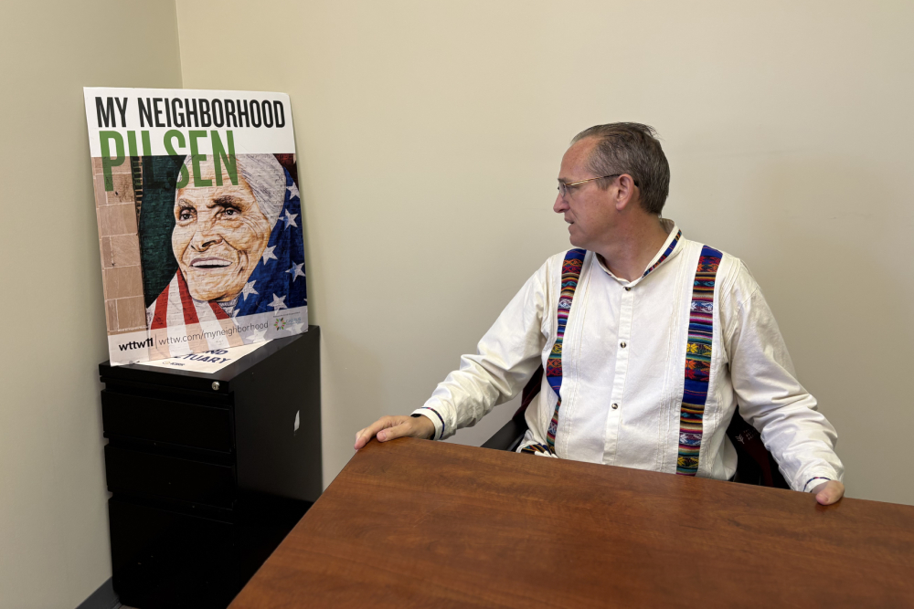 Dominican Fr. Brendan Curran sits at a desk in his office next to a poster of the late Pilsen Catholic activist Micaela “Miquita” Ibarra, Oct. 27, 2025. (NCR photo/Camillo Barone)