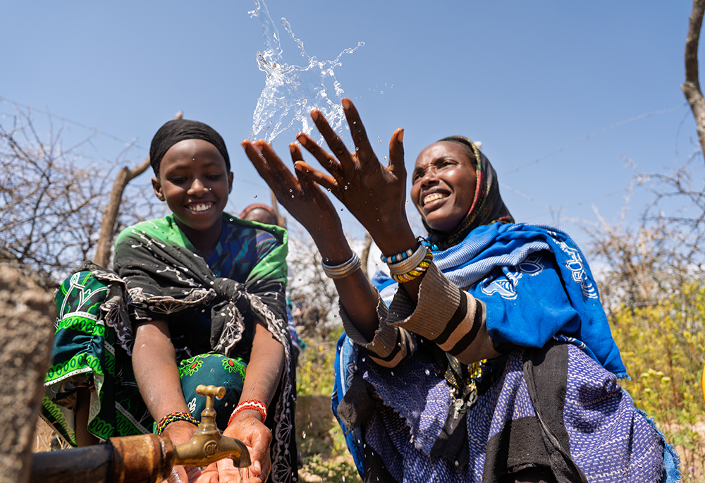 Ware Tune, right, splashes water from a spigot in her village of Kallu Jilo, in northern Ethiopia. The water project was developed by a collaboration of three Caritas organizations, SCIAF, CAFOD and Trócaire. "Clean water has solved a big problem," Tune said. (SCIAF/James Cave)