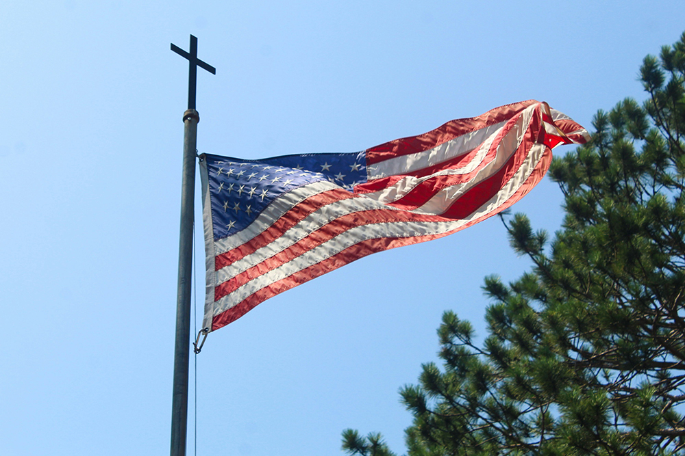Cross on top of flagpole with United States flag flying (Unsplash/Cody Otto)