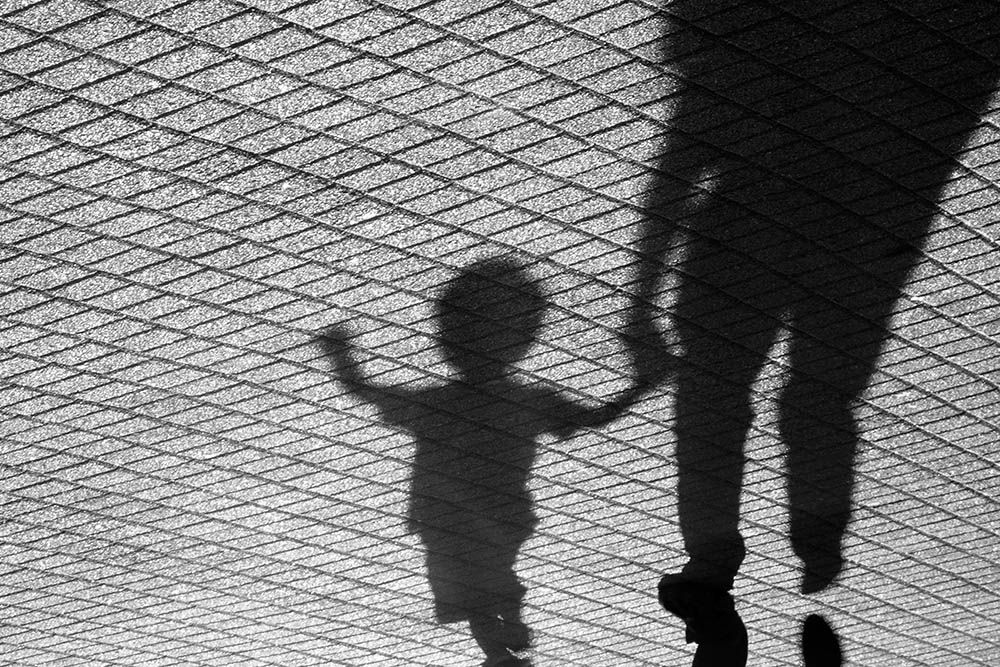 Shadows of a toddler and an adult holding hands walking on a street (Dreamstime/Alexlinch)
