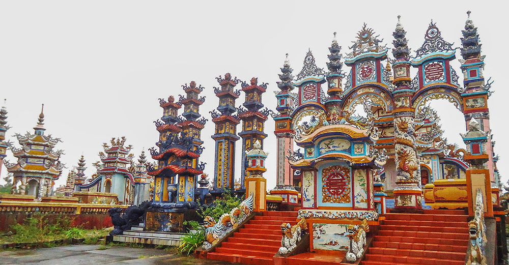An ornate triple gate adorned with delicate carvings marks the entry to a family mausoleum. The structure merges pagoda-style architecture with Confucian and Taoist motifs, embodying harmony between the spiritual and earthly realms. (Joachim Pham)