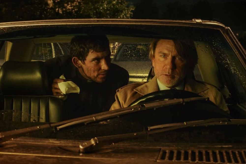 The characters Fr. Jud Duplencity (Josh O'Connor) and Benoit Blanc (Daniel Craig) in a car