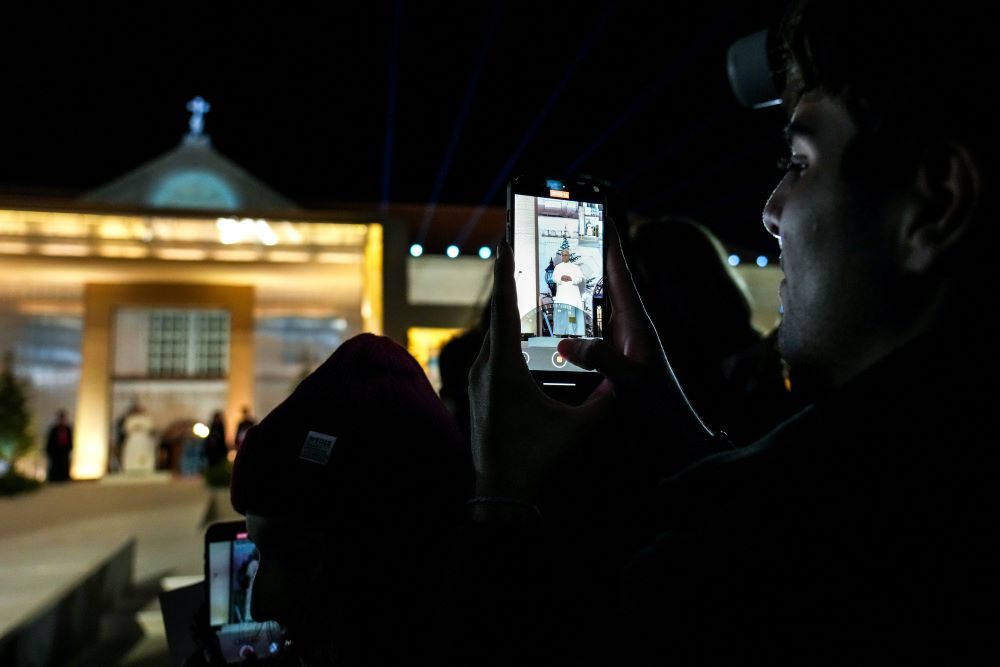 A young man takes a photo of Pope Leo XIV with his phone.