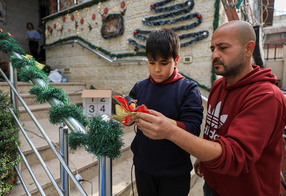 A Palestinian man and boy decorate outside Holy Family Church in Gaza City Dec. 9, 2025, as the community prepared for modest Christmas celebrations after two years of war. Throughout the month of December, Caritas Jerusalem launched the "Christmas of Hope," a campaign meant to address the "deep need to restore joy, dignity, and spiritual renewal to communities that have endured" the devastation of war. (OSV News/Reuters/Dawoud Abu Alkas)