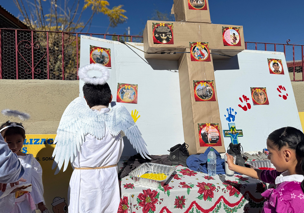 Children taking part in a traditional posada procession along the border wall in Nogales, Mexico, stop by a cross to dip their hands in paint and leave their handprints in a gesture honoring migrants on Dec. 20. (Anita Snow)