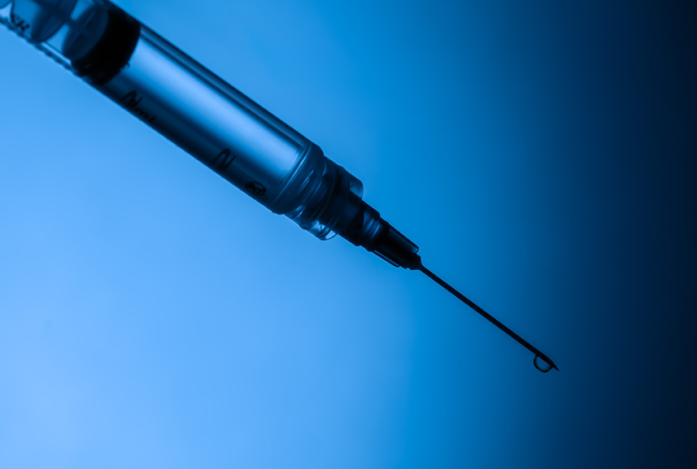 A syringe with a sharp, dripping needle tip against a gradient blue-to-black background