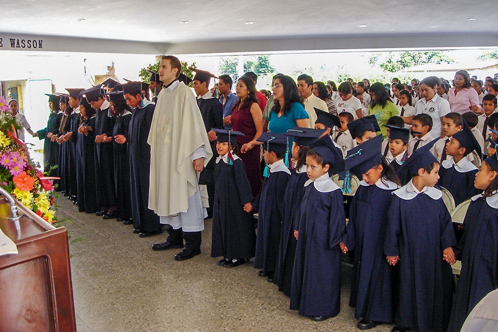 Then-Fr. Ronald Hicks prays with students from Nuestros Pequeños Hermanos in Texistepeque, El Salvador in this photo from a graduation in 2005. Hicks spent five years, 2005-2010, working with the organization for abandoned and vulnerable children. (Courtesy of Nuestros Pequeños Hermanos)