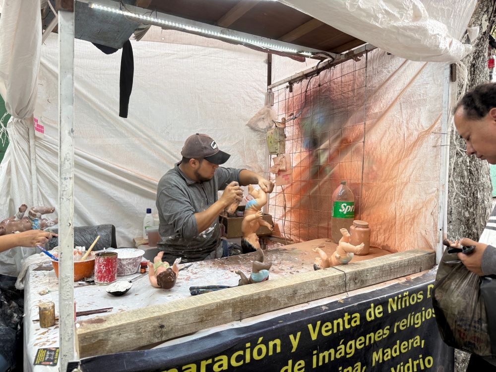 An artisan applies a fresh coat of spray paint to a Baby Jesus figurine Jan. 27 while a customer waits at a Mexico City market that repairs, sells and dresses the plaster representations of the Christ Child to be taken to church for a blessing on Candlemas, celebrated Feb. 2. (Anita Snow) 