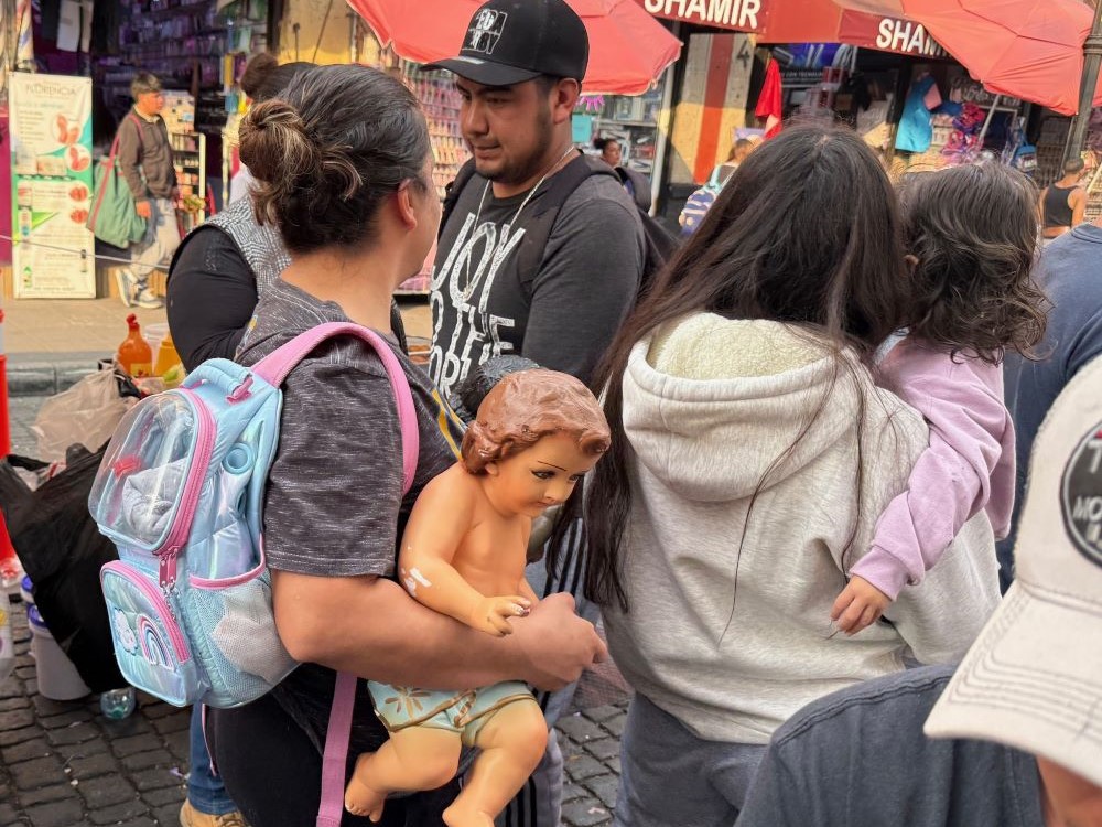 A woman carries her damaged Baby Jesus figurine Jan. 27, next to another woman carrying a toddler, to a Mexico City market that repairs the plaster dolls that represent the Christ Child that are taken to church for a blessing by the priest on Candlemas, celebrated Feb. 2. (Anita Snow)