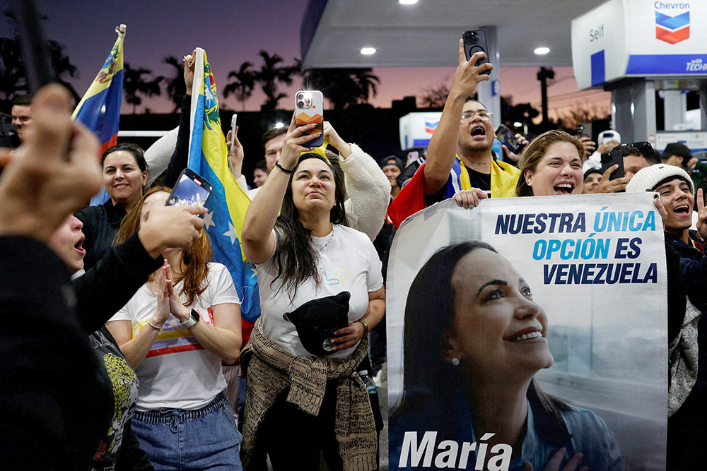 A woman holds a banner depicting Venezuelan opposition leader and Nobel Peace Prize laureate Maria Corina Machado, as people react in Miami Jan. 3, 2026, to the news that U.S. forces struck Venezuela and captured its president, Nicolás Maduro. (OSV News/Reuters/Marco Bello)