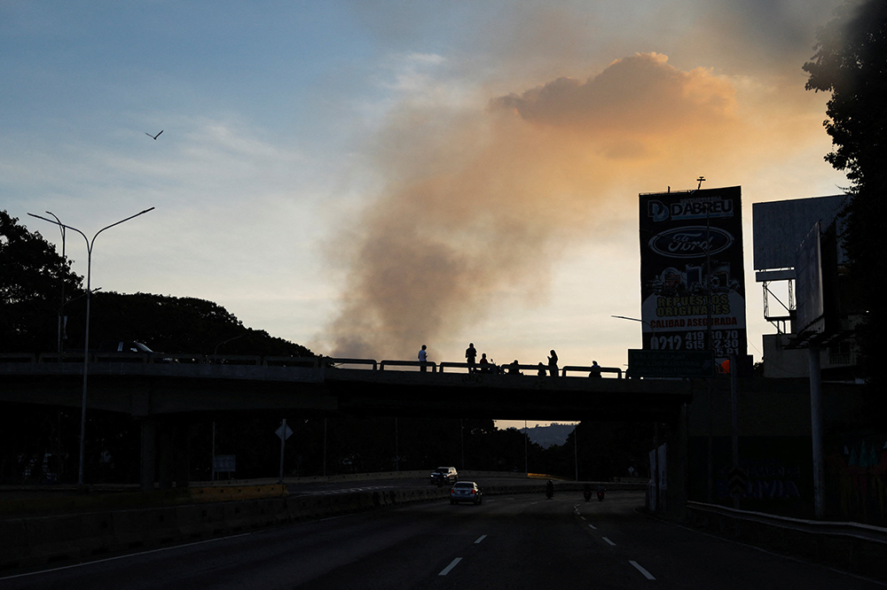 People on a bridge are silhouetted as smoke rises near Fort Tiuna, after U.S. President Donald Trump said the U.S. struck Venezuela and captured its President Nicolás Maduro, in Caracas, Venezuela, Jan. 3, 2026. (OSV News/Reuters/Leonardo Fernandez Viloria)