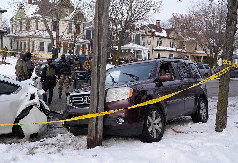 Federal agents gather next to a vehicle with a bullet hole in the windshield after its driver was shot by a U.S. immigration agent, according to local and federal officials, in Minneapolis, Jan. 7, 2026. (OSV News/Reuters/Tim Evans)