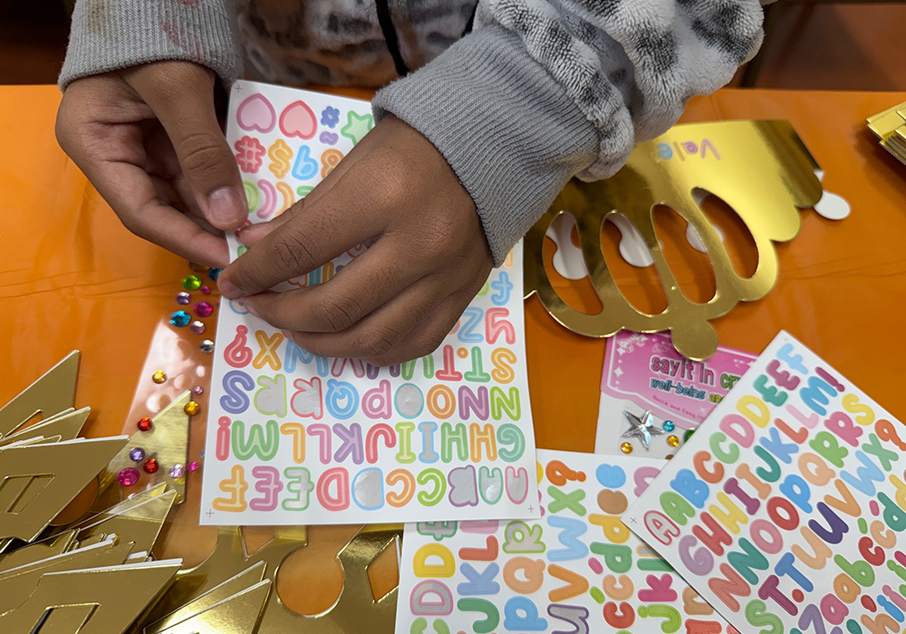 A young migrant boy uses stickers to decorate a golden cardboard crown during a Three Kings Day celebration organized by the advocacy group Salvavision in Tucson, Arizona, Jan. 4, 2026. (Anita Snow)