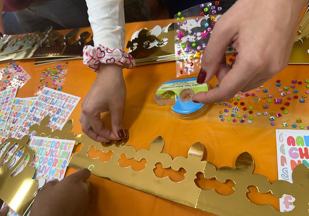 A student nurse volunteer helps a migrant child decorate a golden cardboard crown with stickers during a Three Kings Day celebration organized by Salvavision in Tucson, Arizona on Jan. 4, 2026. (Anita Snow)