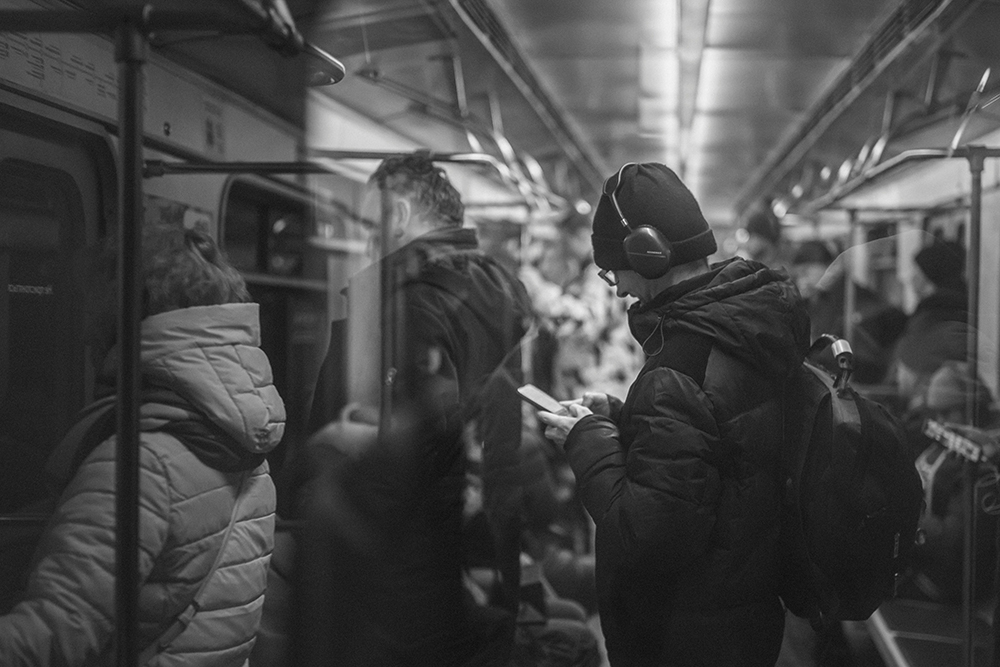 People standing riding the subway, one wearing headphones and looking at a cellphone (Unsplash/Myznik Egor)