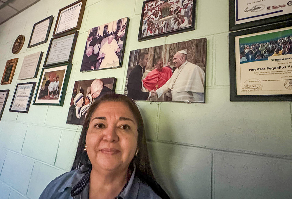 Brenda Méndez, director of programs for Nuestros Pequeños Hermanos in El Salvador, talks about her time working with New York City Archbishop-elect Ronald Hicks on Jan. 19, 2025, in Texistepeque, El Salvador, with photos of him in the background. Hicks spent five years in the country as the organization's regional director for Central America. Méndez said that he arrived at the site to listen and to support staff. (NCR photo/Rhina Guidos) 