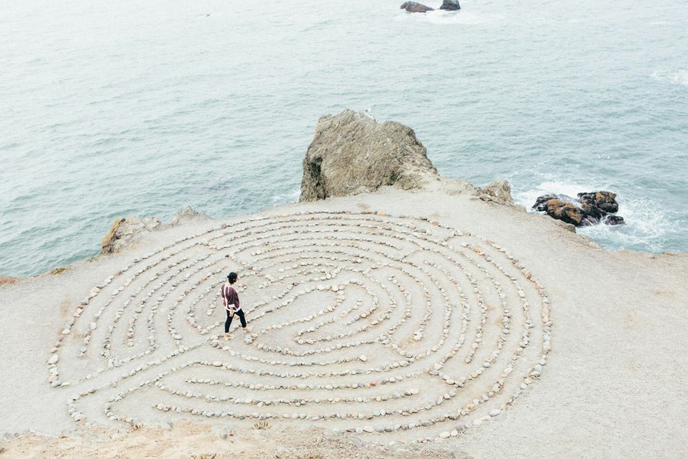 A person walks a labyrinth created by rocks near water's edge.