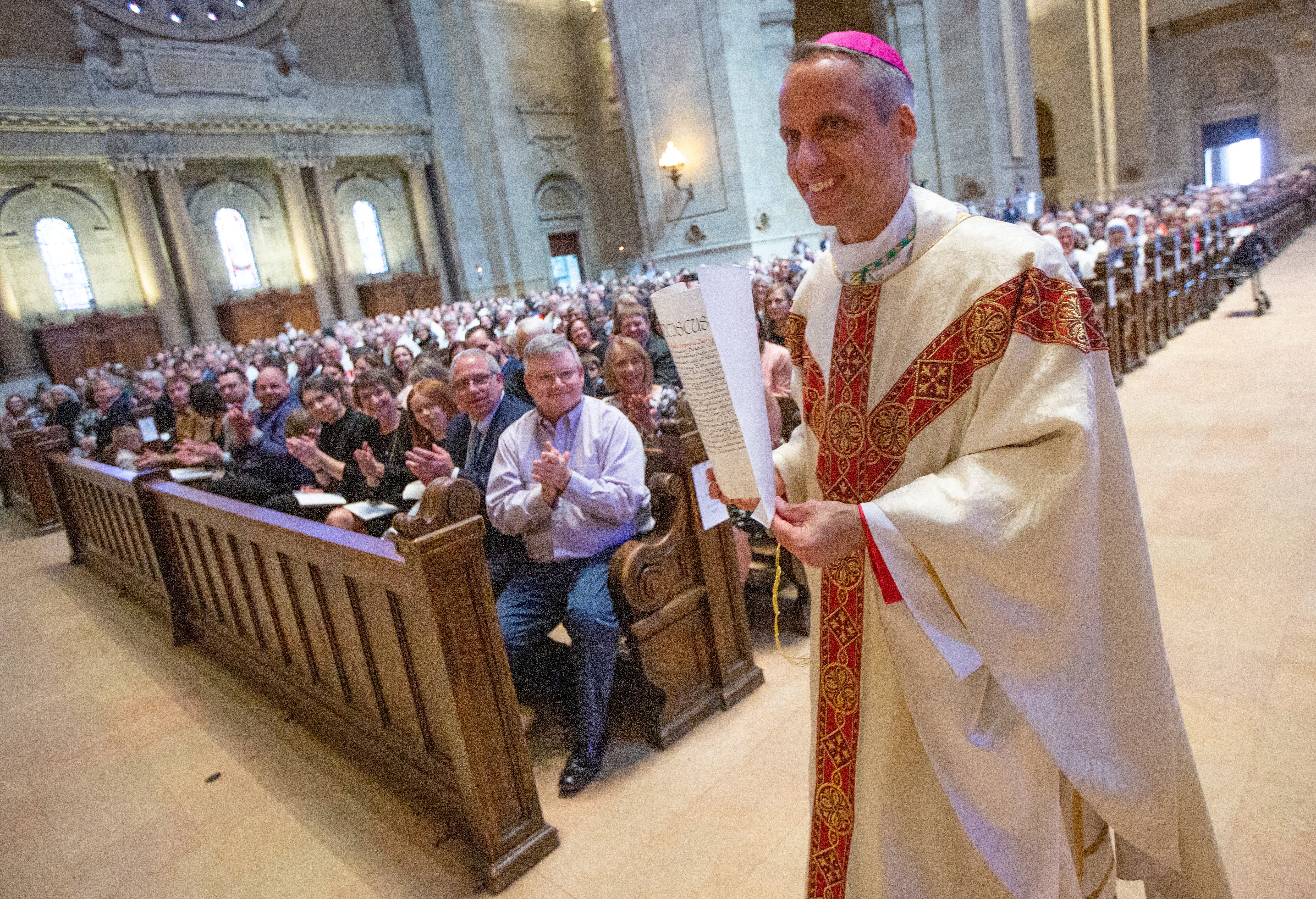 Auxiliary Bishop Michael Izen shows the papal mandate from the Apostolic See as he walks through the Cathedral of St. Paul in St. Paul, Minnesota, during his episcopal ordination April 11, 2023. (OSV News/Catholic Spirit/Dave Hrbacek)