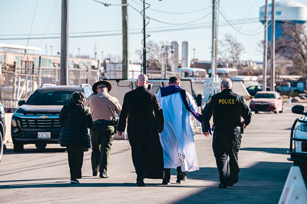 Scalabrinian Fr. Leandro Fossá, pastor of Our Lady of Mount Carmel Parish (second from right); Claretian Fr. Paul Keller, missionary priest and provincial leader (center); and Sr. Alicia Gutierrez, a member of the congregation of the Society of Helpers (left) walk toward the ICE Broadview detention center escorted by two officers on Feb. 18, 2026. (Courtesy of Coalition for Spiritual and Public Leadership/Derek Carter)