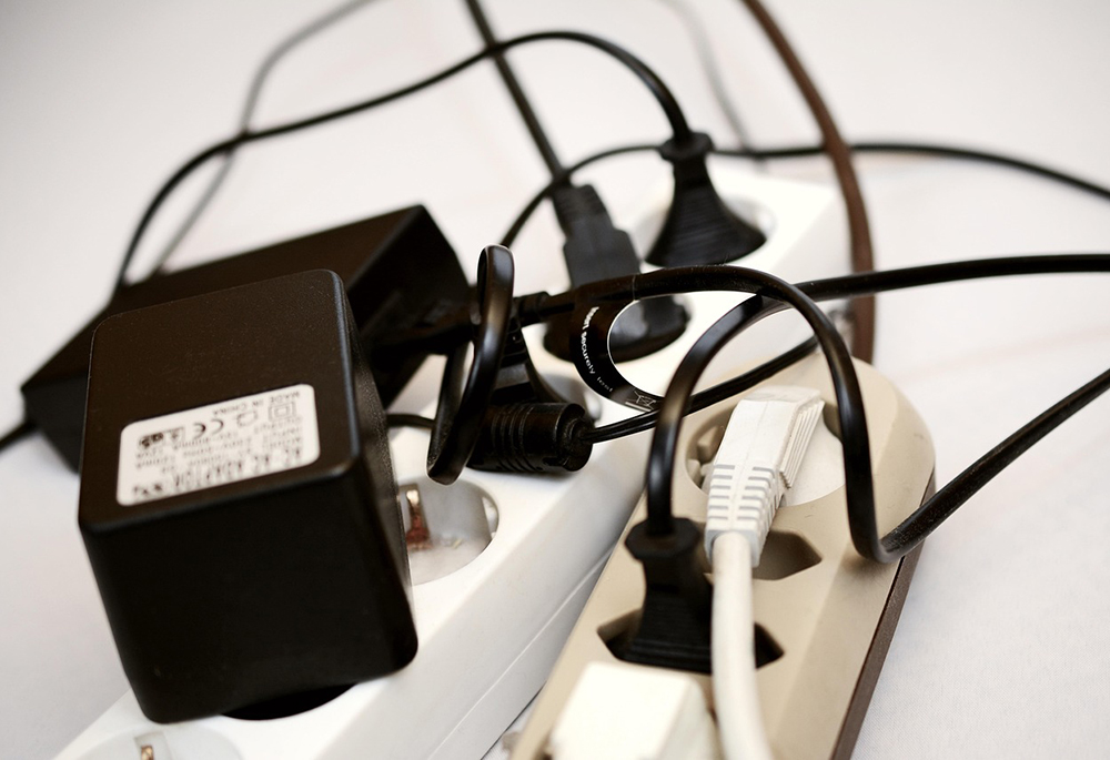 Several black and white electrical cords are plugged into two power strips that lay on a white surface in this photo illustration. (Pixabay/congerdesign)