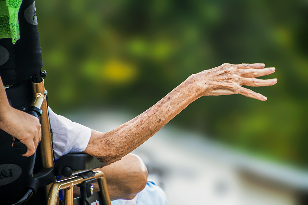 The hand of an elderly person in a wheelchair reaches out. (Pixabay/truthseeker08)