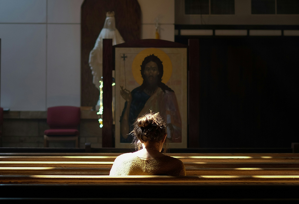A woman sits in a church pew in front of an icon of Jesus and a statue of Mary (Unsplash/Josh Applegate)