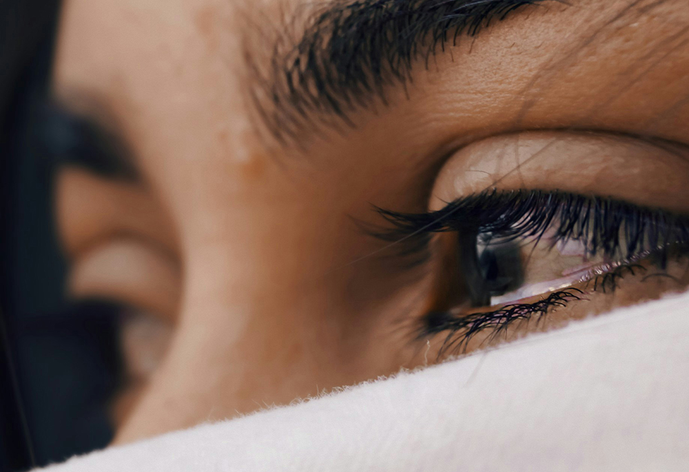 A close-up shows a woman's eyes, which are tearing up. (Unsplash/Louis Galvez)