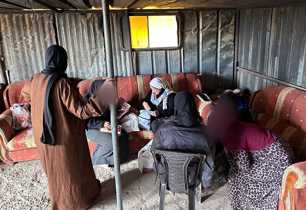 Mujeres se reúnen en el campamento beduino de Tabana, cerca de Al-Azariyeh, en Cisjordania, para participar en un taller de bordado titulado "Hilos de paz", el 28 de febrero de 2026, como parte del acompañamiento de las hermanas combonianas a las comunidades beduinas que viven en la incertidumbre diaria. En la foto aparece la Hna. María Cecilia Sierra Salcido, con velo blanco, en el centro. La imagen está difuminada para proteger su identidad. (Foto: cortesía Hna. María Cecilia Sierra Salcido)