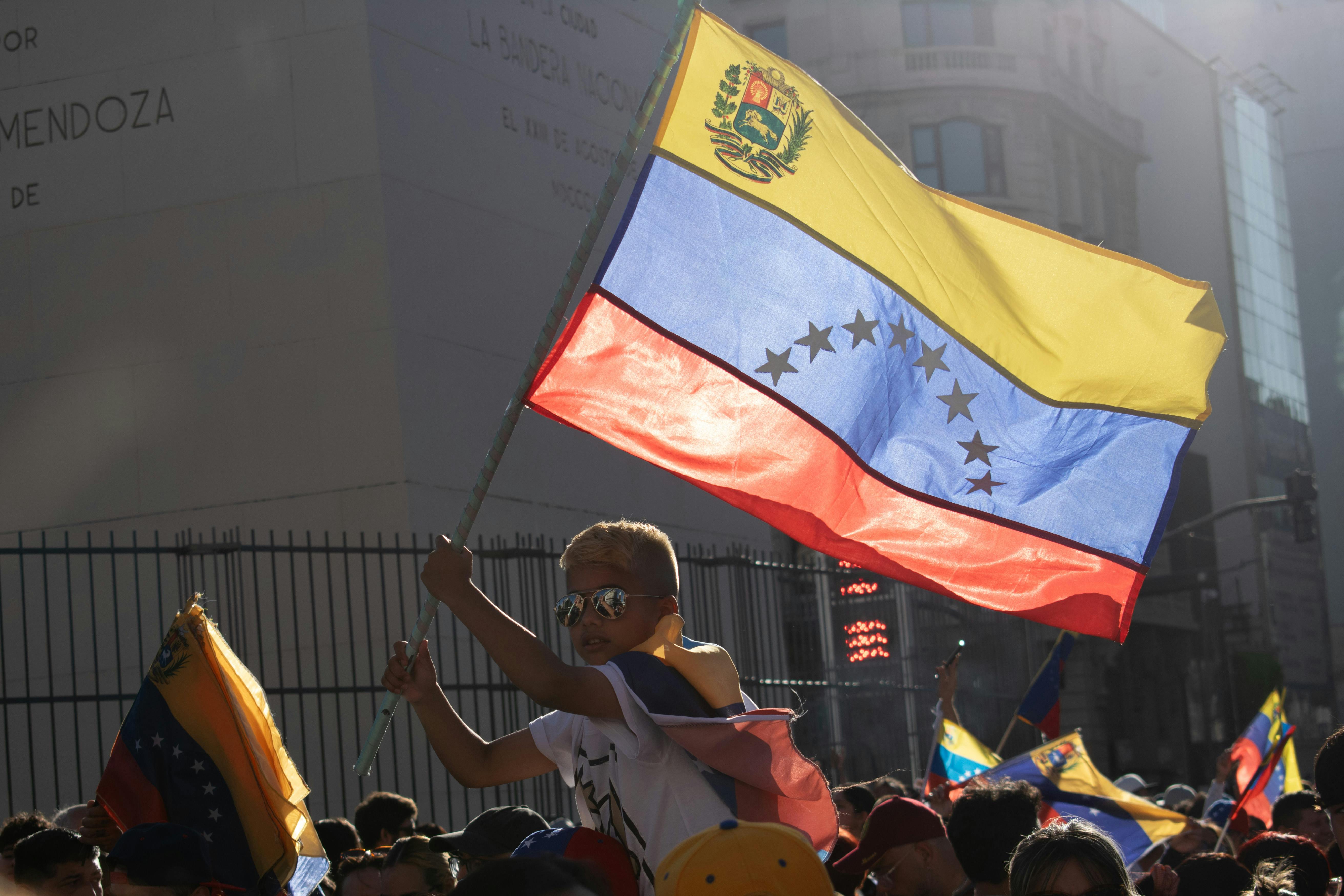 A child holds the Venezuelan flag during a protest in Buenos Aires, Argentina. The Venezuelan crisis has led hundreds of thousands of children to grow up far from their homeland. (Pexels/Renan Braz)