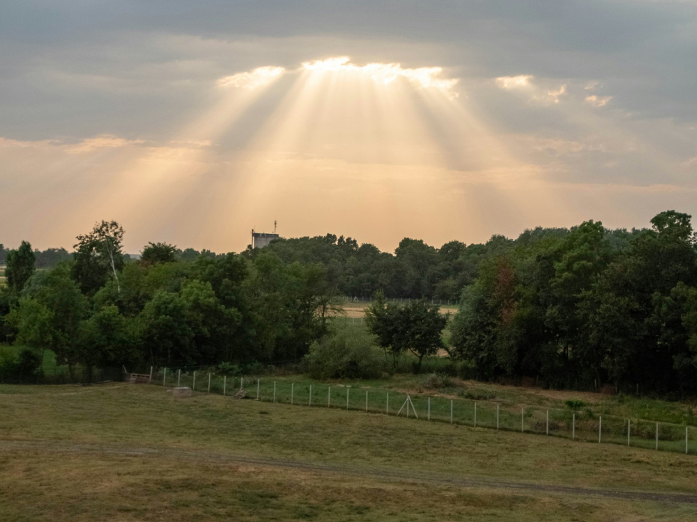 Rays of sunlight shining through clouds over a green field.