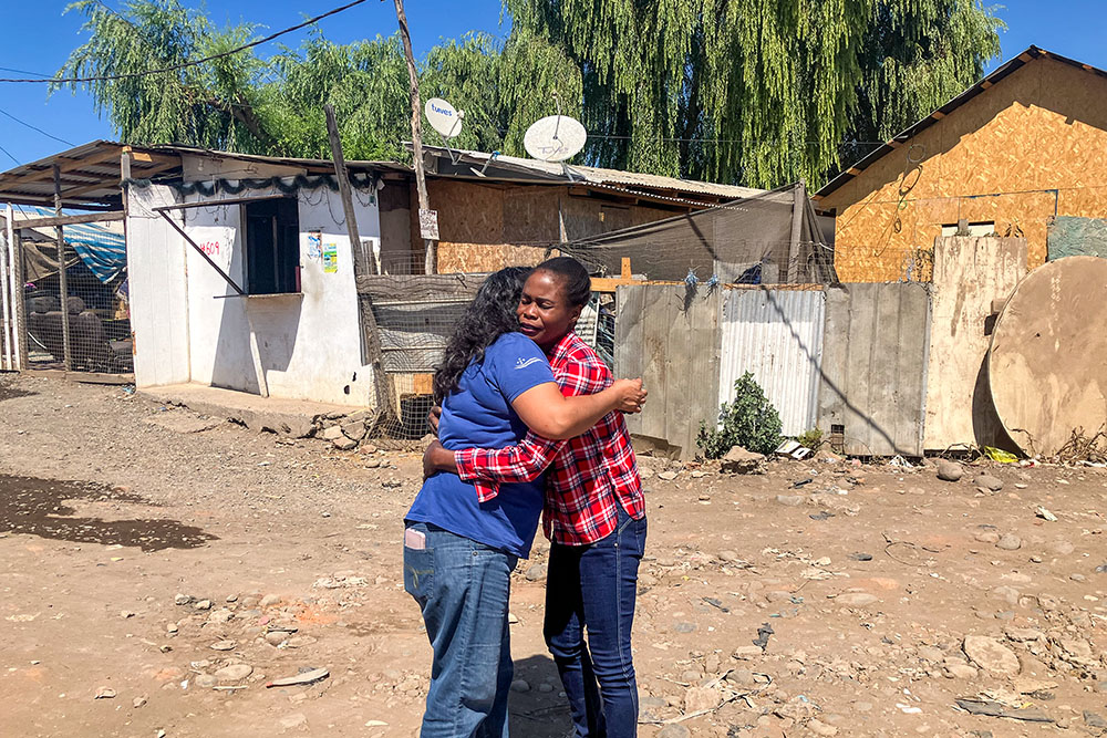 La Hna. Ana María Carvajal saluda a Evena Promesse en las calles de un asentamiento irregular poblado por inmigrantes haitianos en Curicó, Chile. Los residentes del asentamiento se enfrentan a un futuro incierto, ya que el nuevo Gobierno de Chile ha prometido expulsar a los migrantes sin estatus legal. Desde su llegada en 2022, Promesse no ha podido obtener los documentos de inmigración adecuados. (Foto: GSR/David Agren)