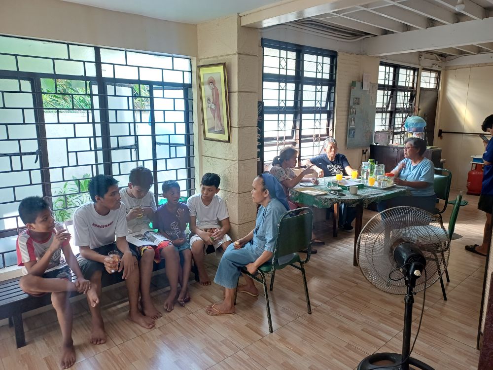 Srs. Maria Elizabeth de Jesus (left) and Cecilia Grace de Jesus, both in blue, sit with neighbors and children inside their modest house in Mandaluyong, Philippines, where the Little Sisters of Jesus live among the communities they accompany. (Oliver Samson)