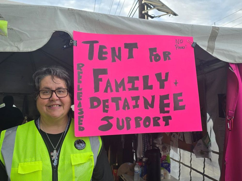 Sr. Susan Rose Francois of the Sisters of St. Joseph of Peace poses next to the sign outside the family and detainee support tent in front of Delaney Hall in Newark, New Jersey. (Courtesy of Eyes on ICE NJ/Joseph O'Leary)