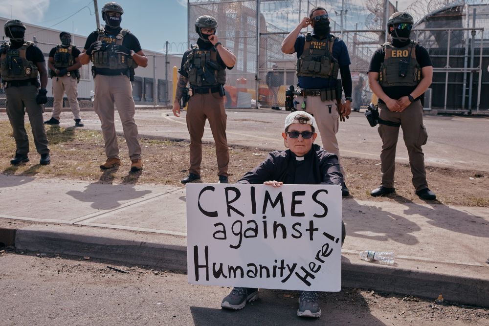A protester holds a sign as ICE agents stand guard outside the Delaney Hall detention during a protest against the transfer of detainees on May 26, 2026, in Newark, N.J. For the past year, volunteers have been present every visiting day to staff the "Radical Hospitality" tent or to peacefully stand vigil outside the facility on non-visiting days. (AP/Andres Kudacki)