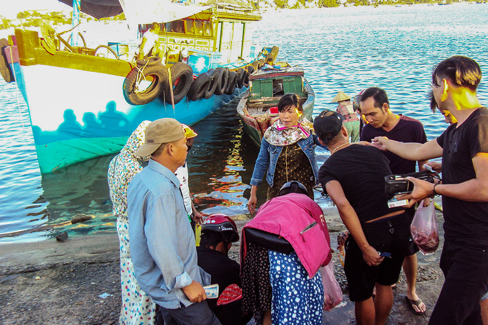 Mary Magdalene Vu Thi Tue (center, in denim jacket) sells fish to customers in Quang Tri, Vietnam, on April 22, 2026. At left is the fishing boat her family recently repaired after years of abandonment following the Formosa disaster. (Reporter in Vietnam)